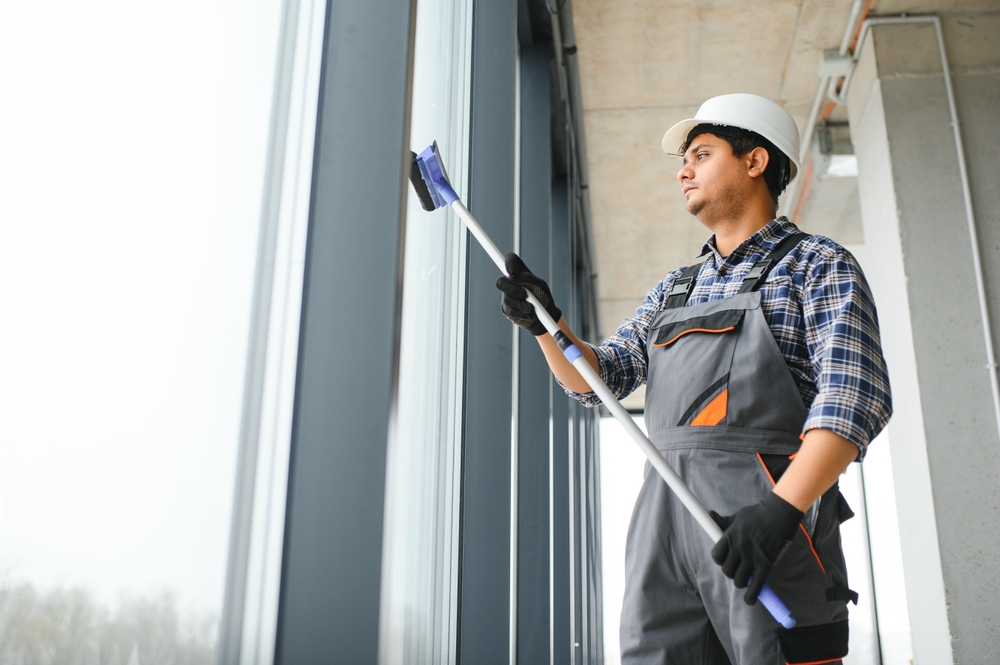 Male professional cleaning service worker in overalls cleans the windows and shop windows.