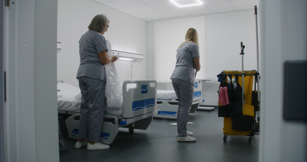 Mature cleaner with her colleague changes bedding on beds.