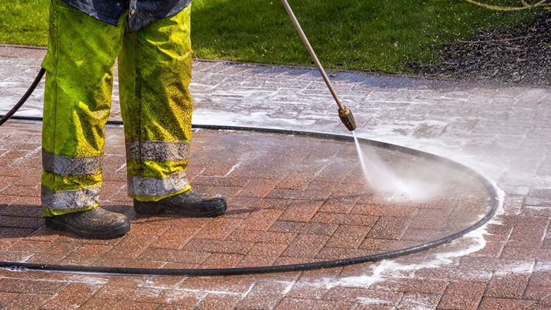 Worker in Yellow Protective Clothing Pressure Washing Monoblock Brick Paver Driveway