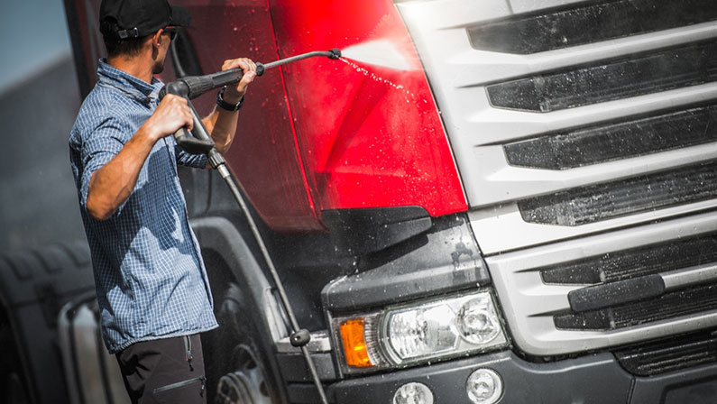 Truck Driver Washing His Semi Truck Tractor. Sunny Day in the Transportation Base.
